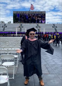 Michael Tynan pictured in the graduate seating area of Husky Stadium in full cap and gown with sunglasses, celebrating his graduation.