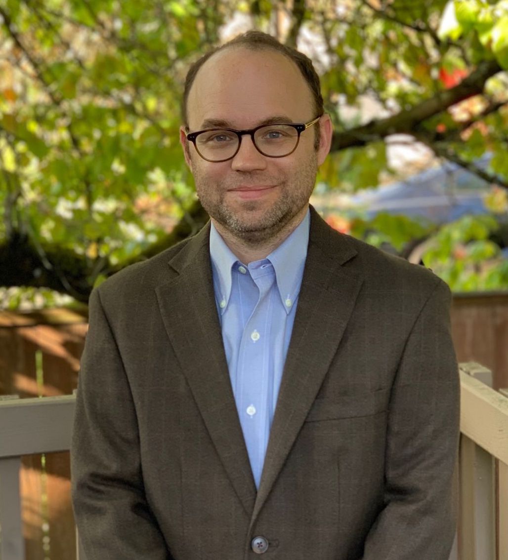 Michael Tynan stands in front of a green tree for a photo wearing a sport coat.