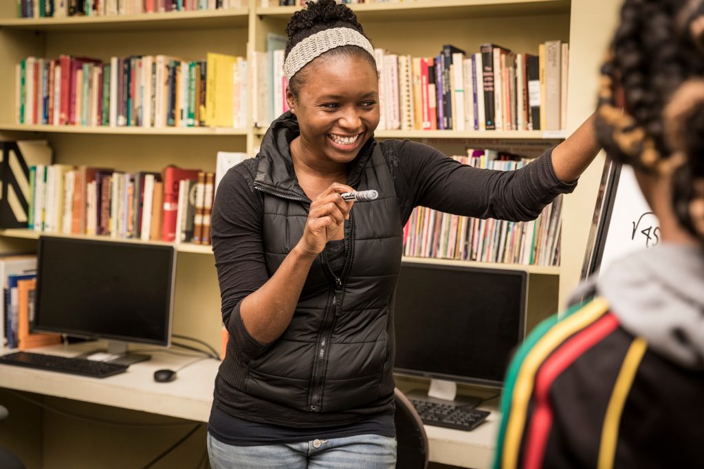 a female student holds a dry erase marker, smiling in conversation with another student